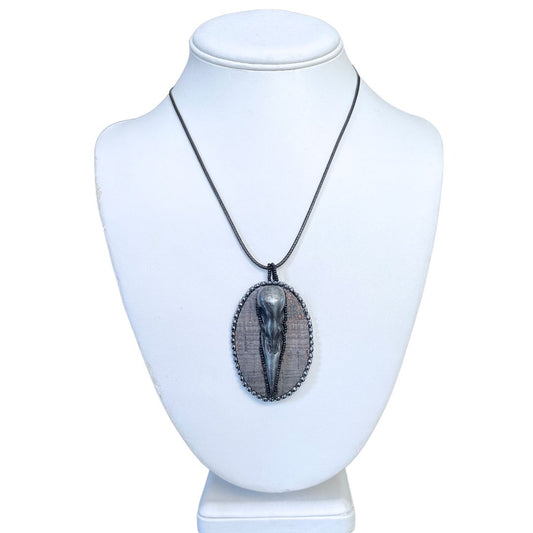 An oval pendant with a polymer clay crow skull on gray cork and hand beaded with silver and black seed beads on a display mannequin