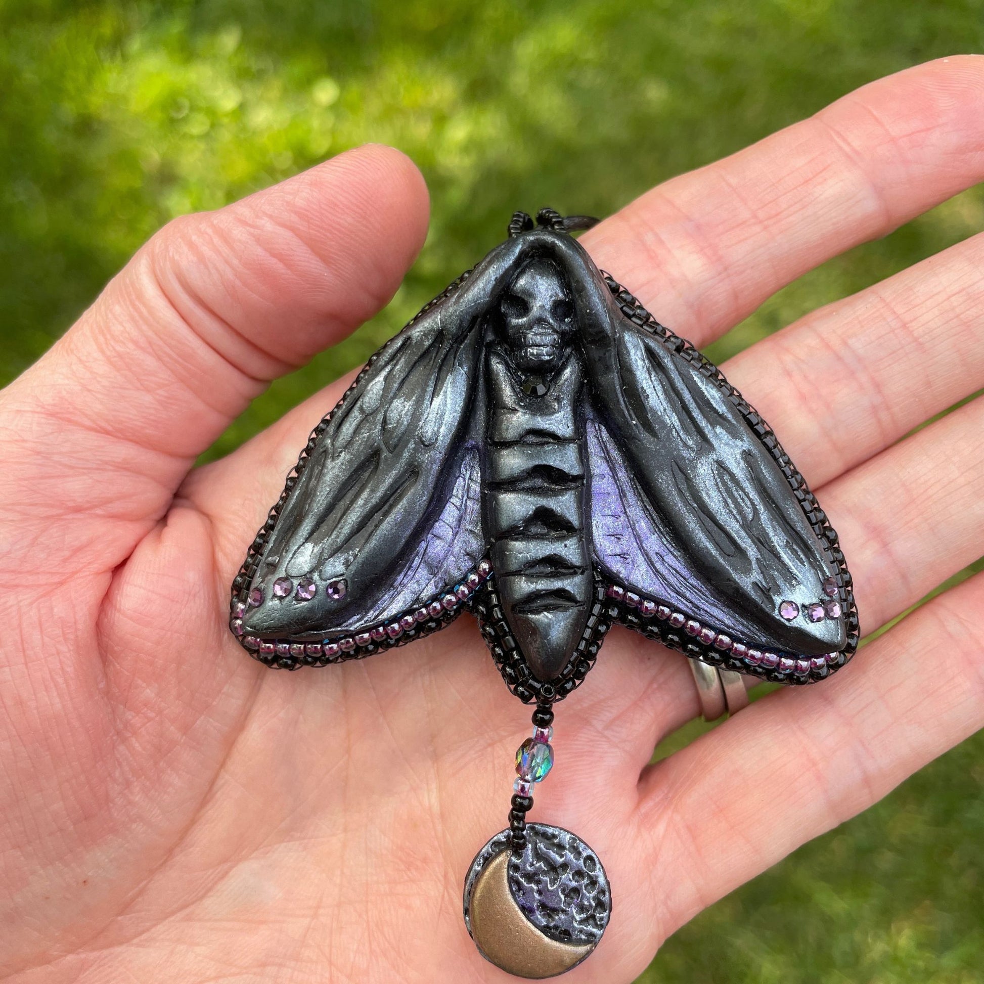 Silver and purple Death Head Moth pendant made with black polymer clay with a round charm with a crescent moon in model's hand