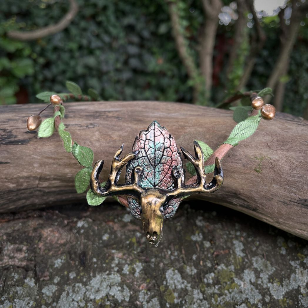 A wire crown with green leaves and a polymer clay leaf and elk focal on a tree branch.