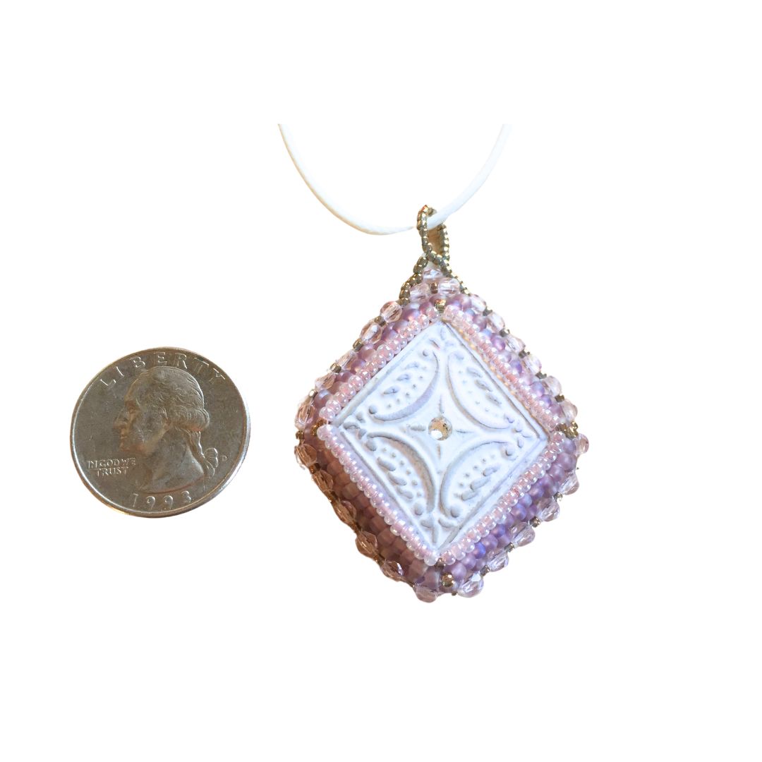 lilac beaded diamond shaped necklace on a white background next to a quarter for size reference.