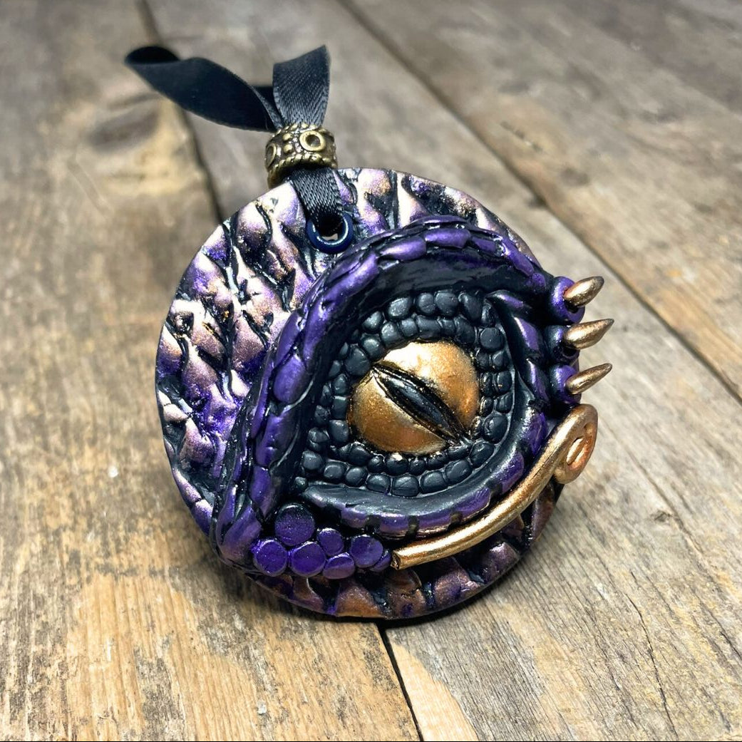 Purple and gold pendant with a black ribbon on a wooden surface