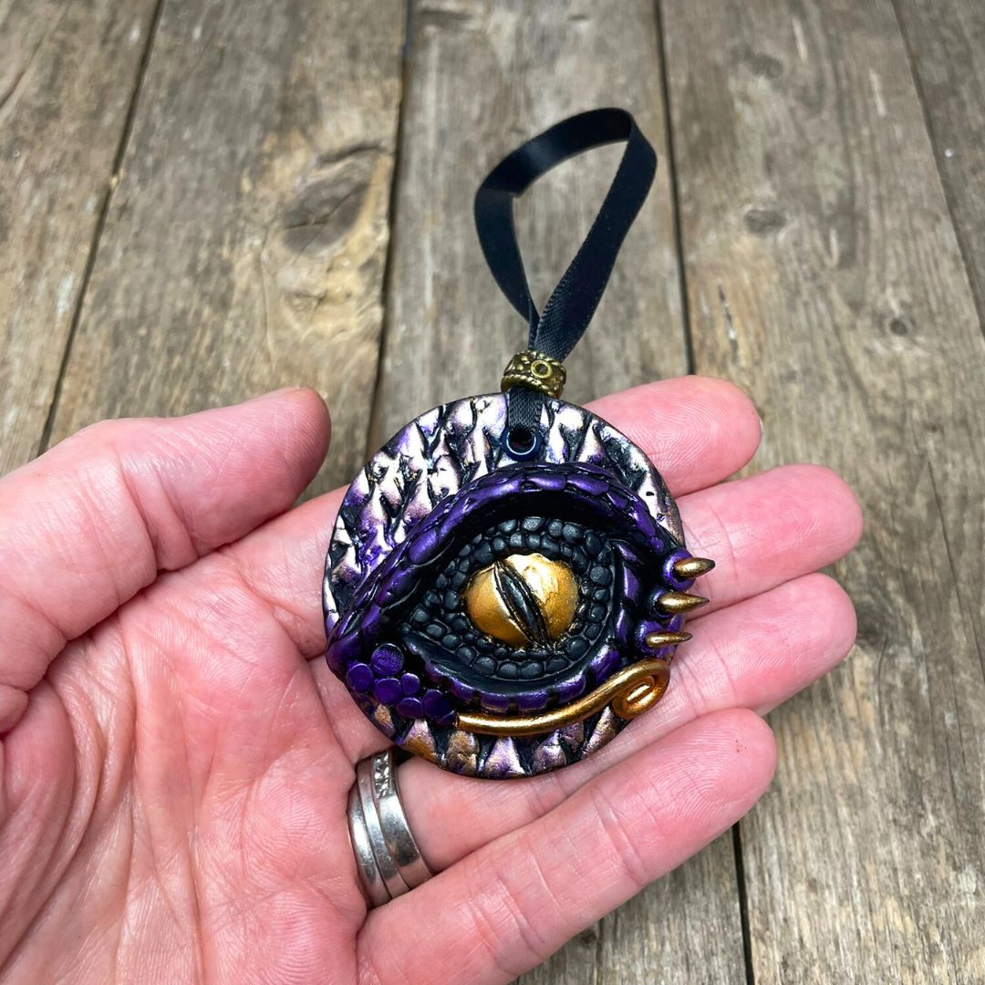 Decorative eye-shaped pendant held in a hand on a wooden surface