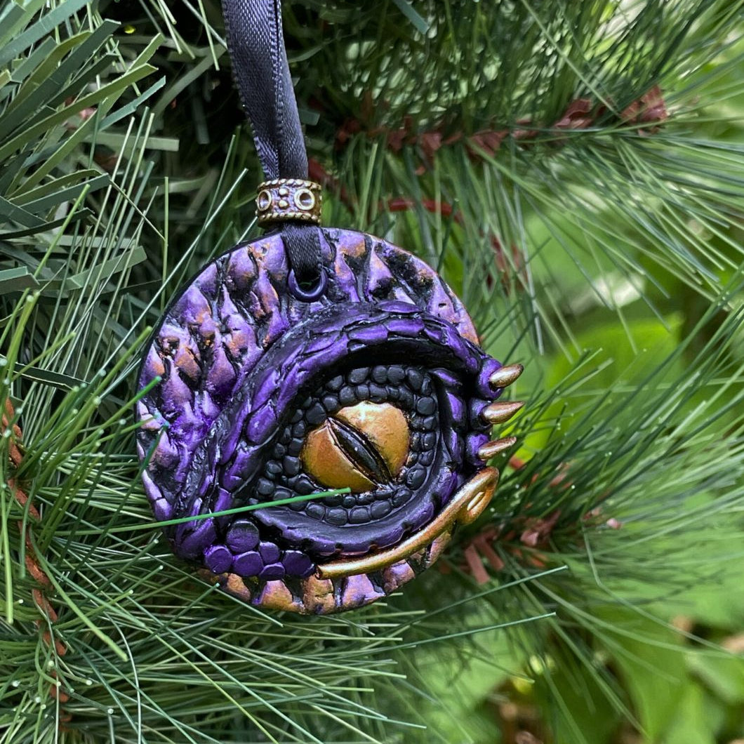 Decorative purple and gold ornament hanging on a green pine branch