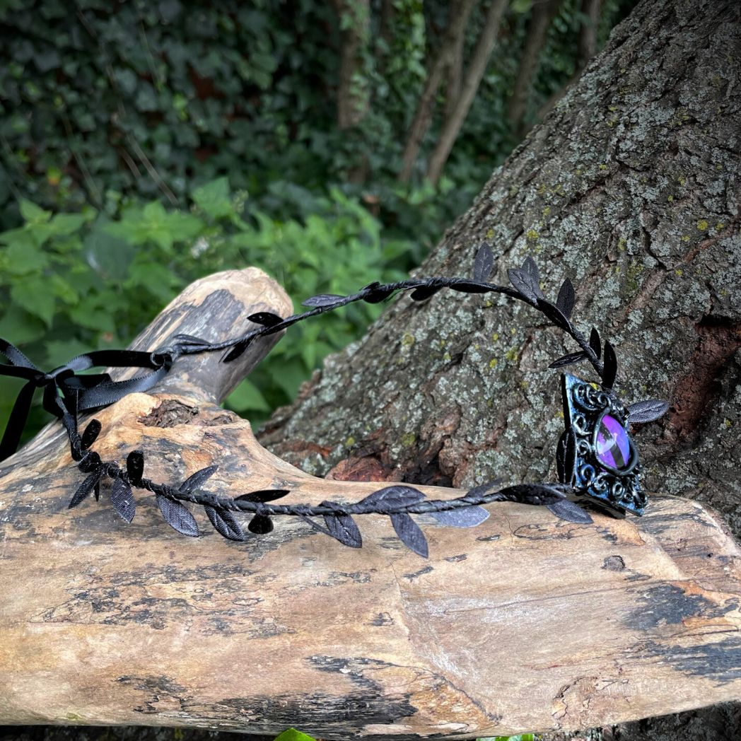 Purple dragon on a diamond shape textured clay base on a black leaf wire headband resting on a tree branch.