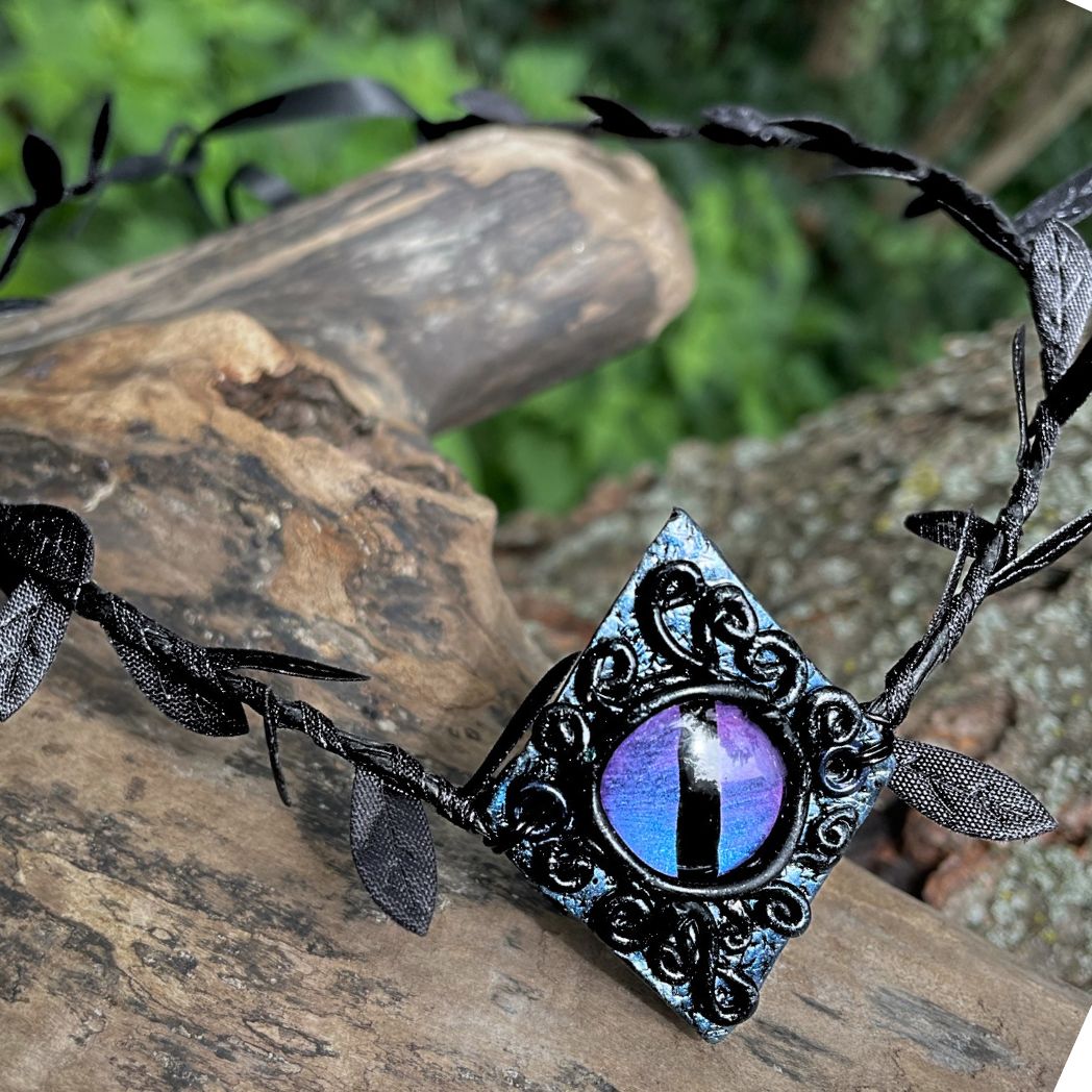 Purple dragon on a diamond shape textured clay base on a black leaf wire headband resting on a tree branch.