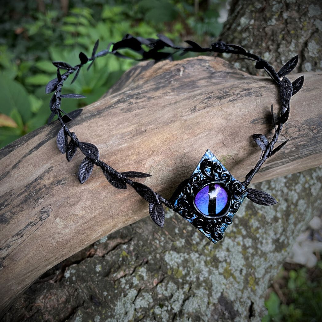 Purple dragon on a diamond shape textured clay base on a black leaf wire headband resting on a tree branch.