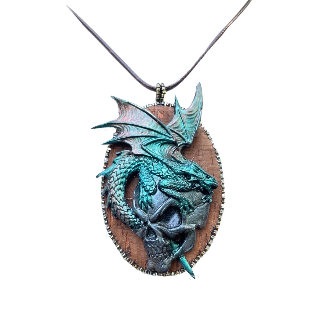 Oval  pendant with a polymer clay green dragon upon a silver fierce skull.