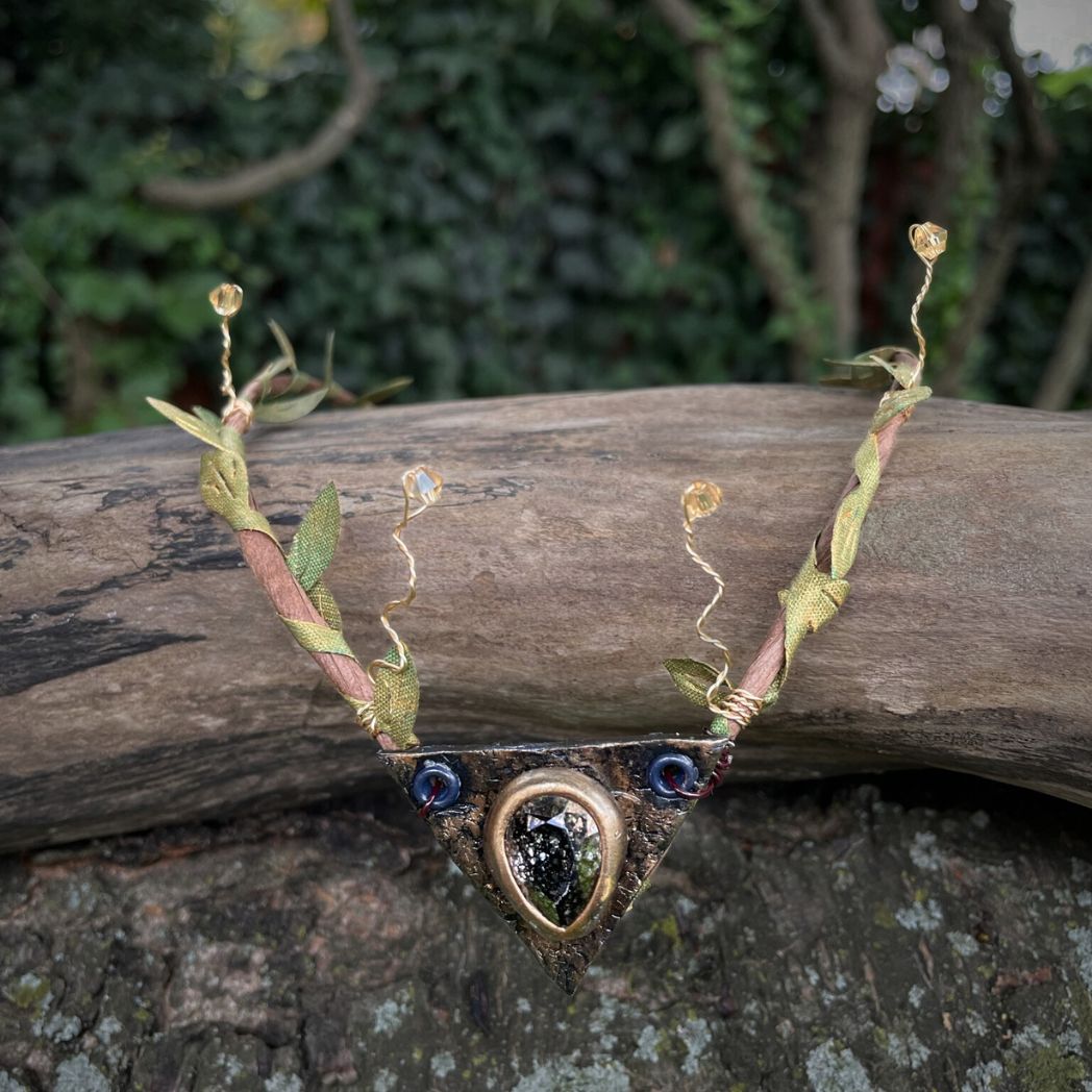 Teadrop crystal focal crwon with brown branches and green fabric leaves. Wired crystals around the sides. Crown sitting on a tree branch.