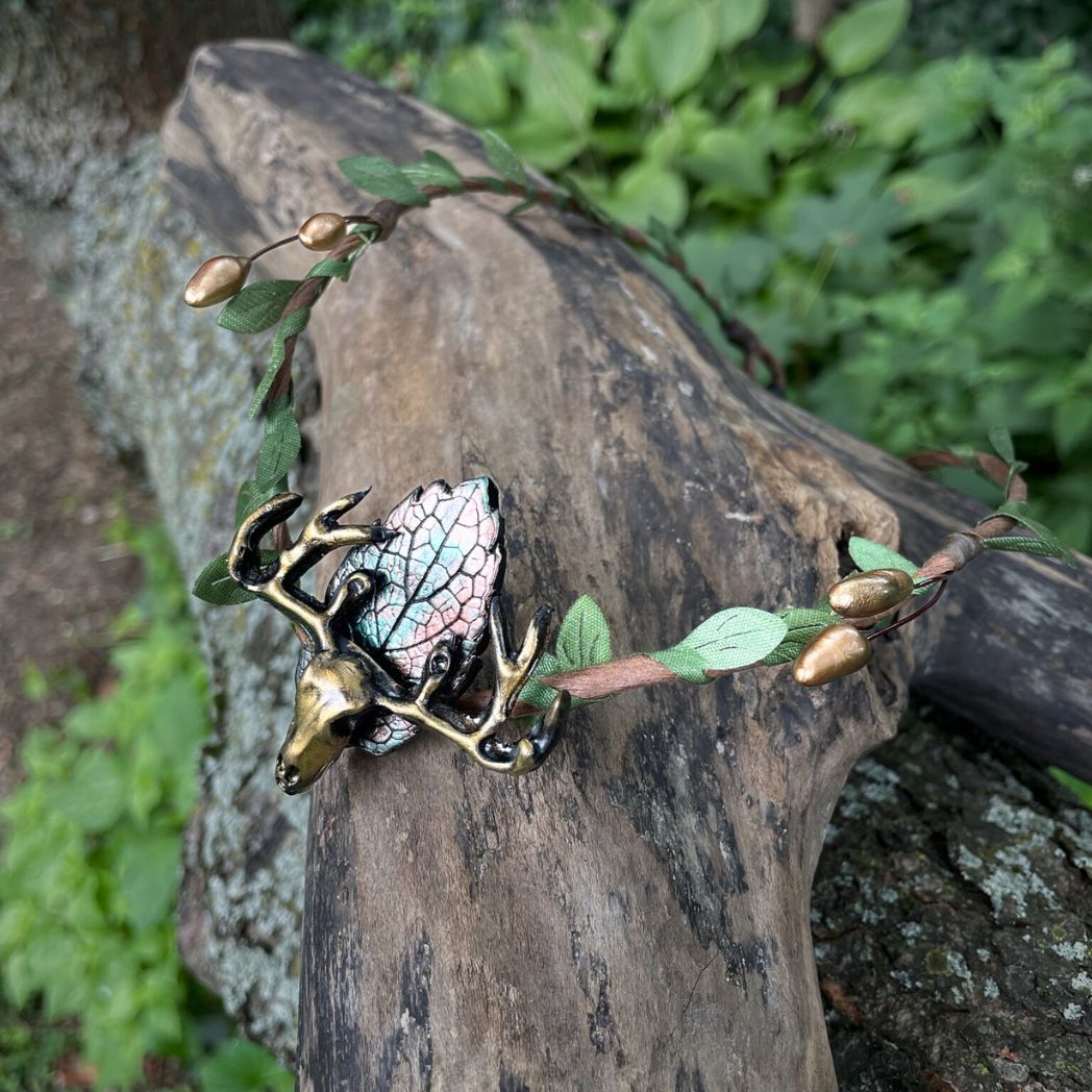 A wire crown with green leaves and a polymer clay leaf and elk focal on a tree branch.