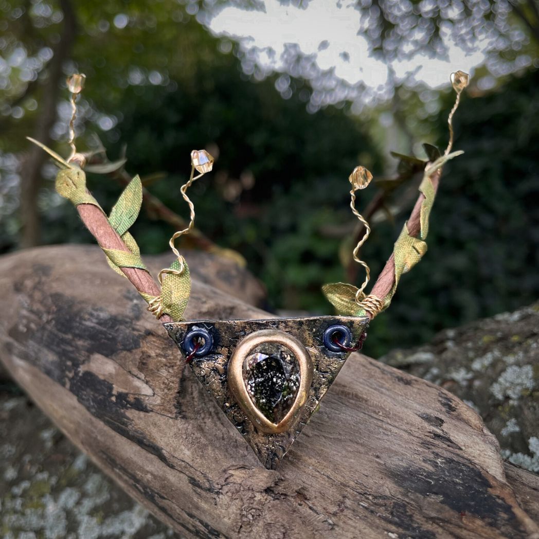 Teadrop crystal focal crwon with brown branches and green fabric leaves. Wired crystals around the sides. Crown sitting on a tree branch.