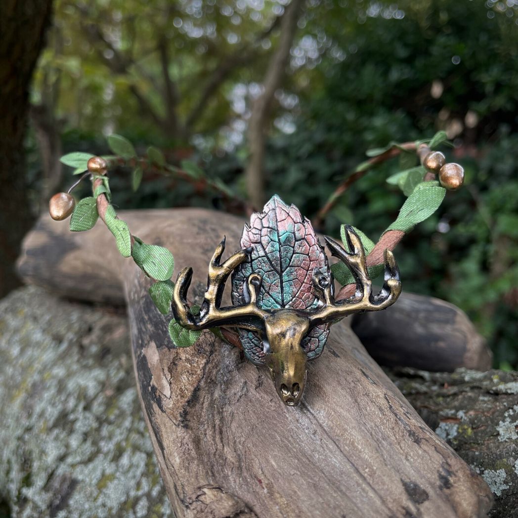 A wire crown with green leaves and a polymer clay leaf and elk focal on a tree branch.