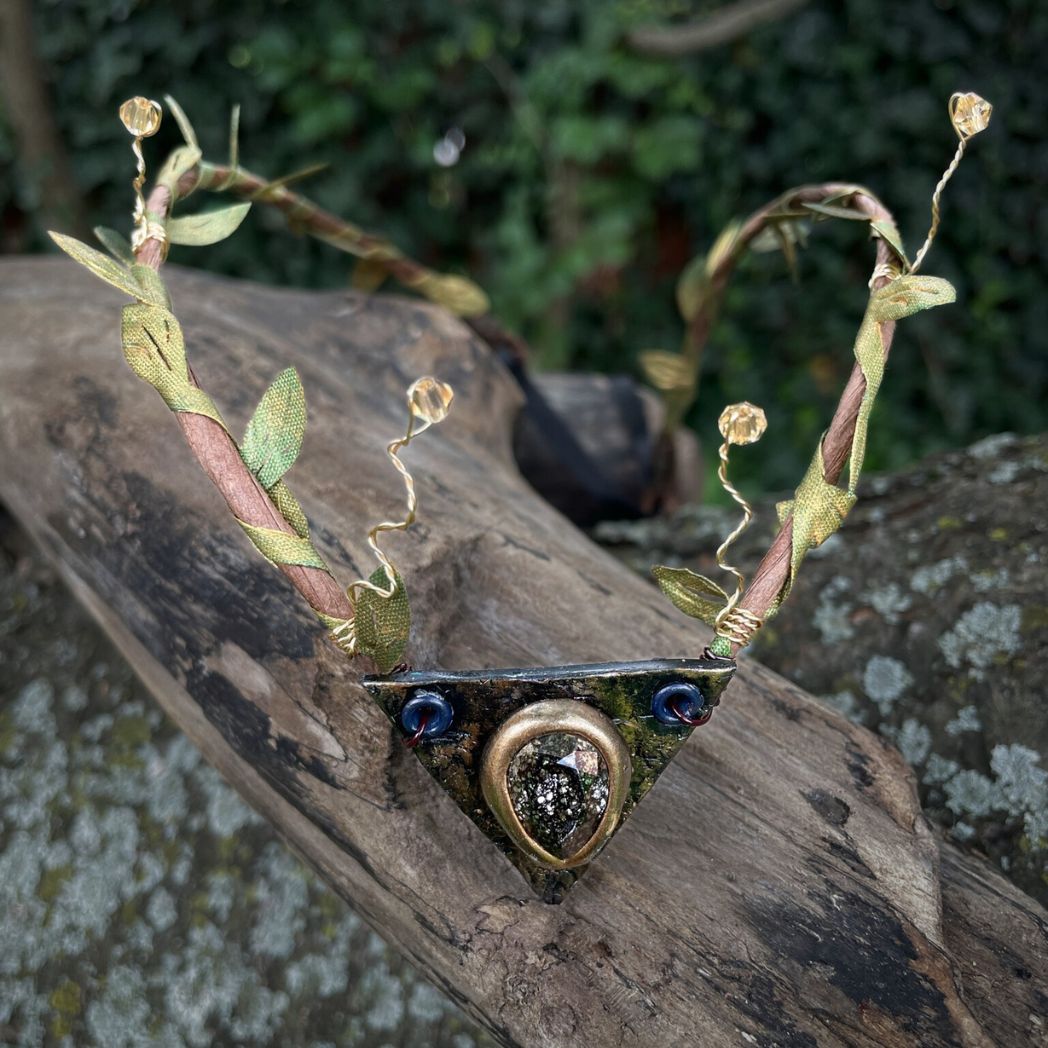 Teadrop crystal focal crwon with brown branches and green fabric leaves. Wired crystals around the sides. Crown sitting on a tree branch.