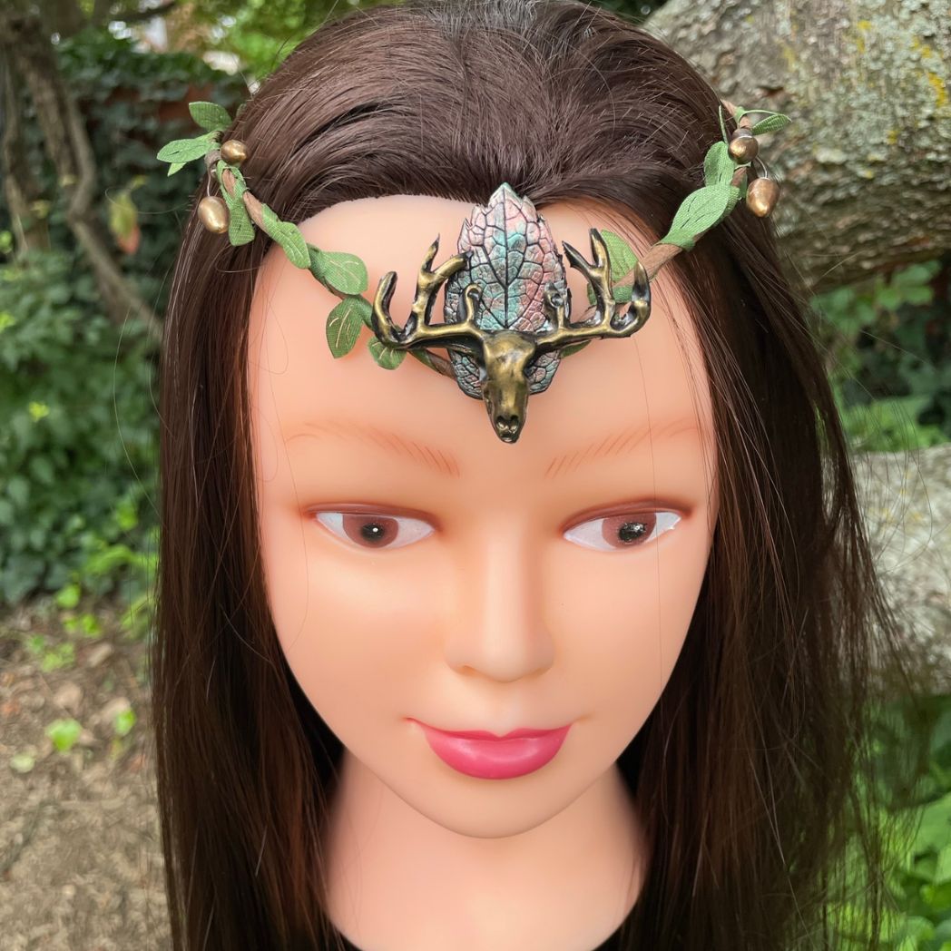 A wire crown with green leaves and a polymer clay leaf and elk focal on a model.