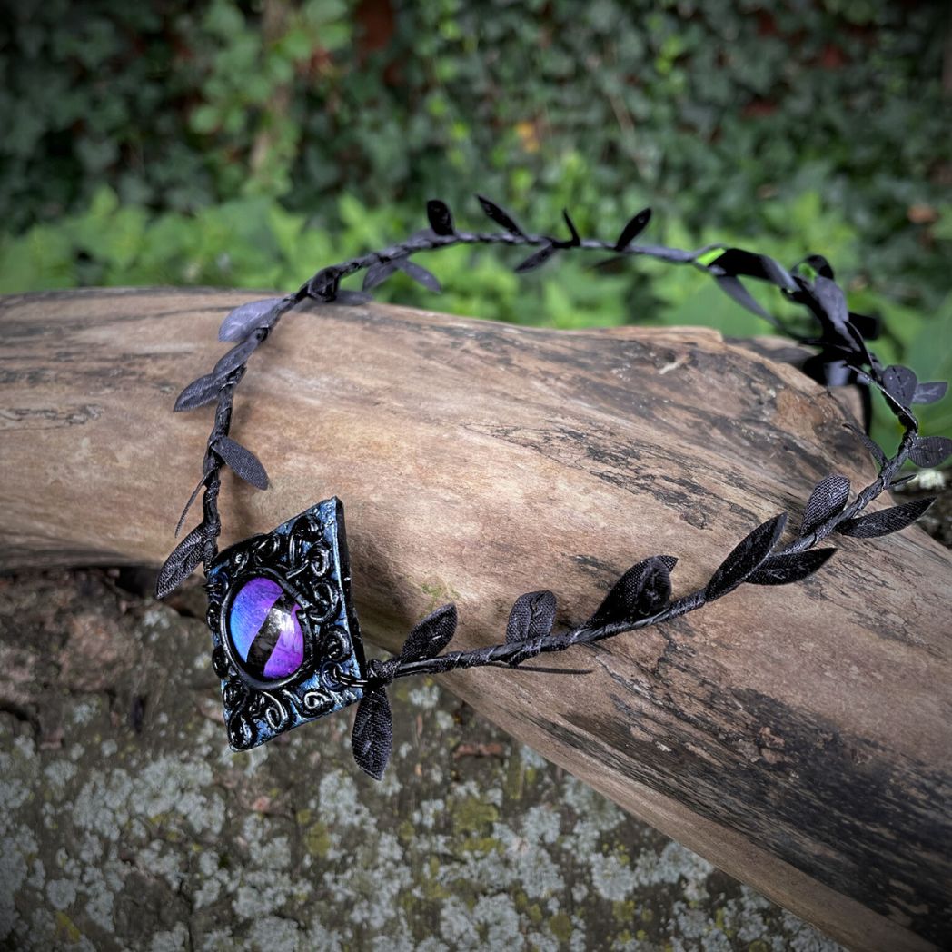Purple dragon on a diamond shape textured clay base on a black leaf wire headband resting on a tree branch.