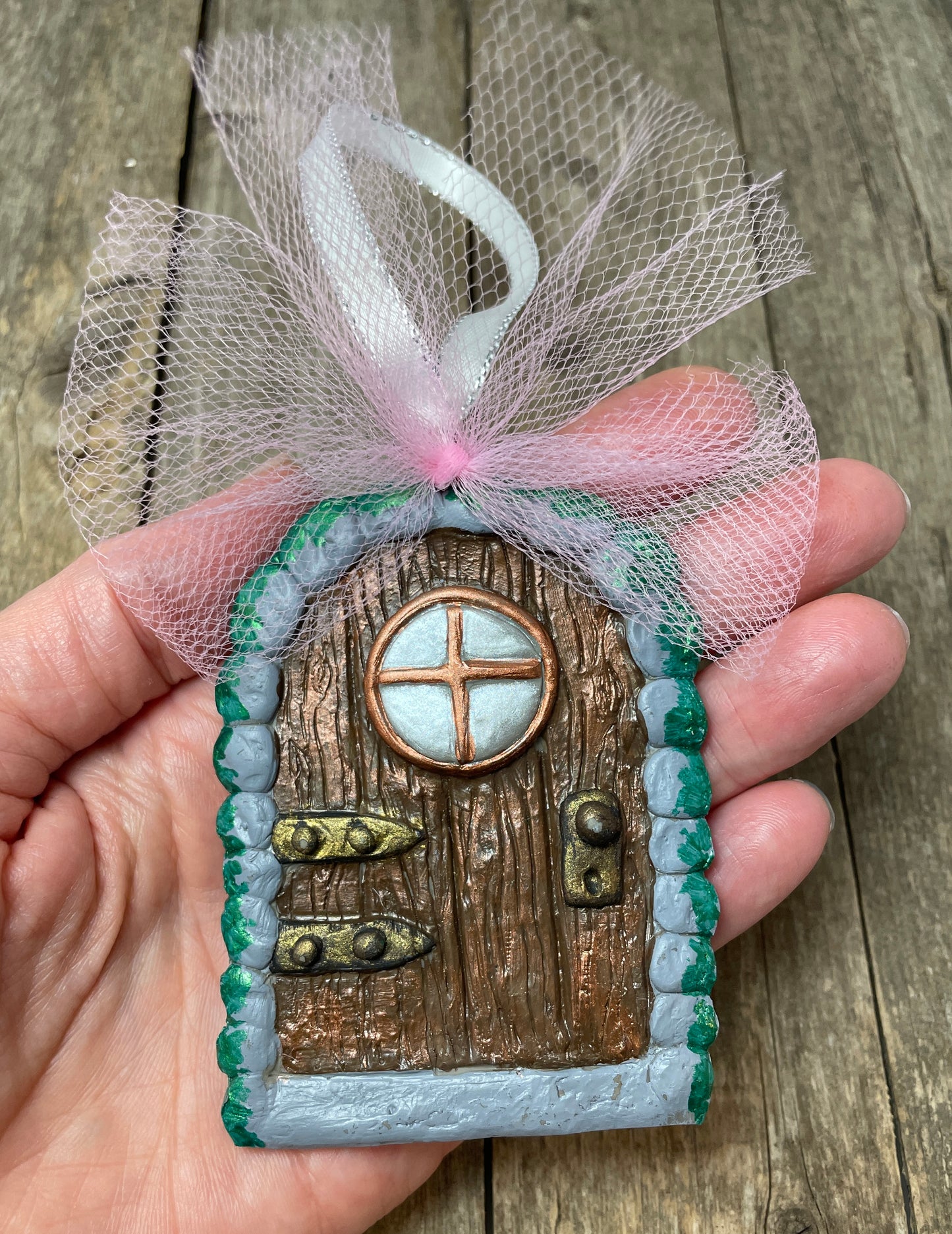 small fairy door ornament with pink tulle bow held in a hand for size reference.