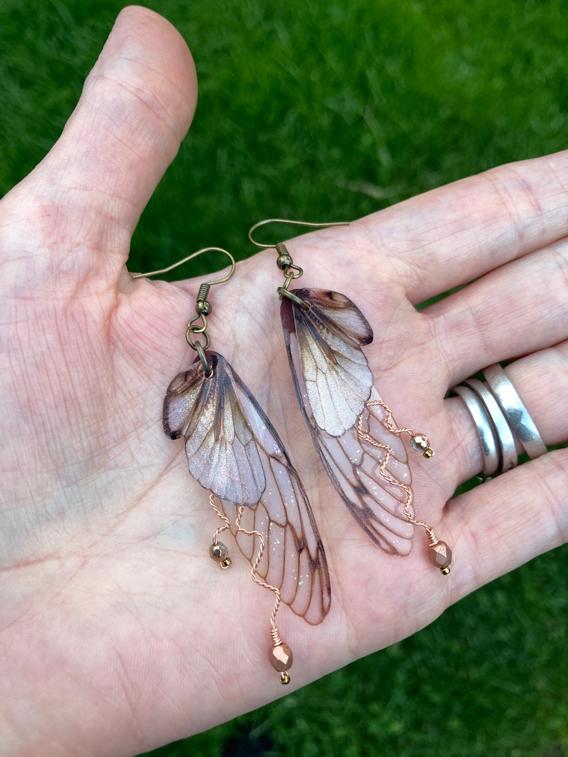 Brown double wing earrings with copper wired branches with crystals laying flat on a hand for size reference