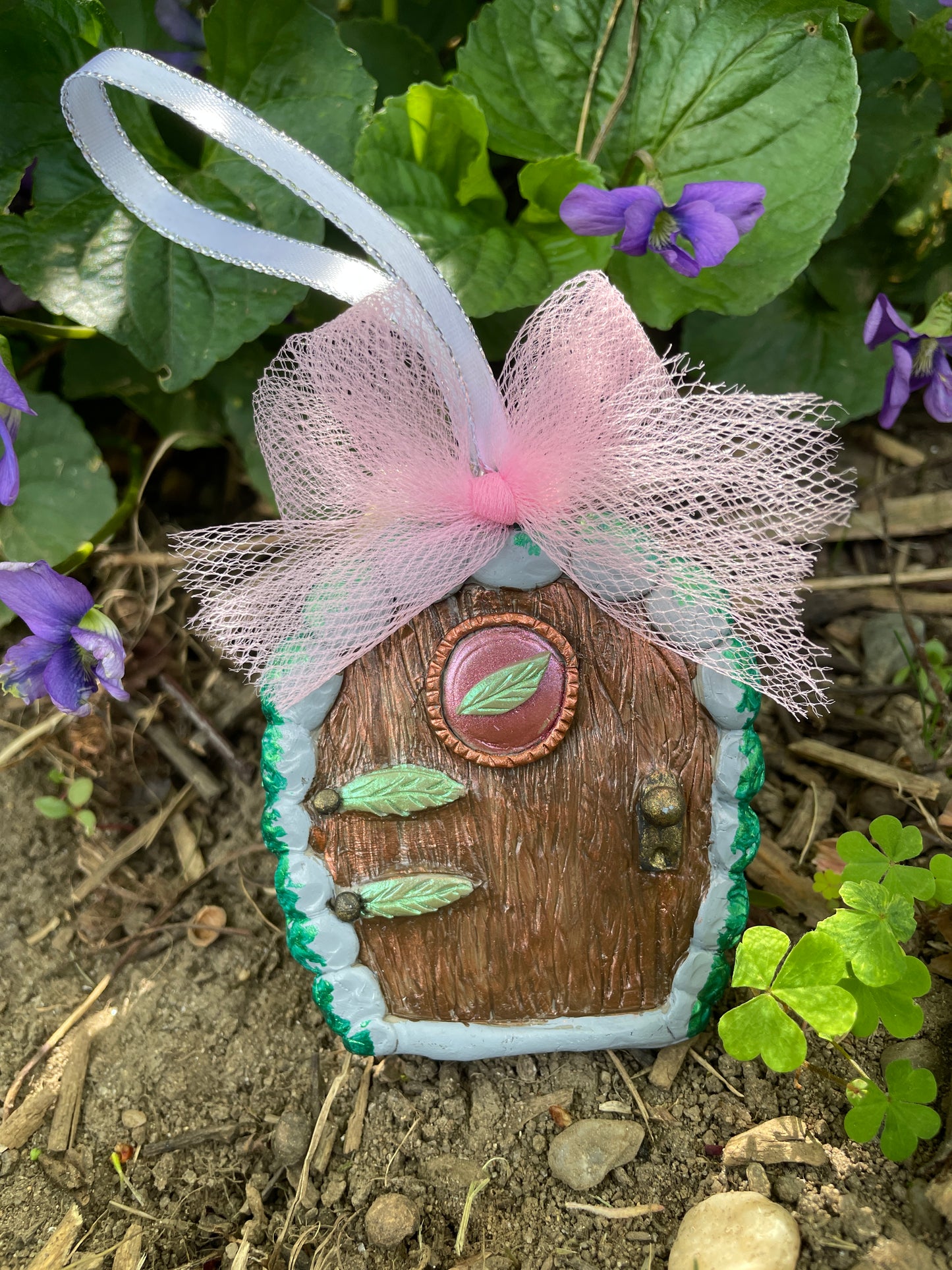 Elven fairy door ornament with leaf motif and pink tulle bow in a garden setting.