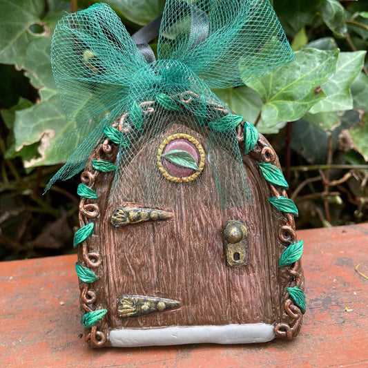 Fairy door ornament with vines and green tulle bow in a garden setting.