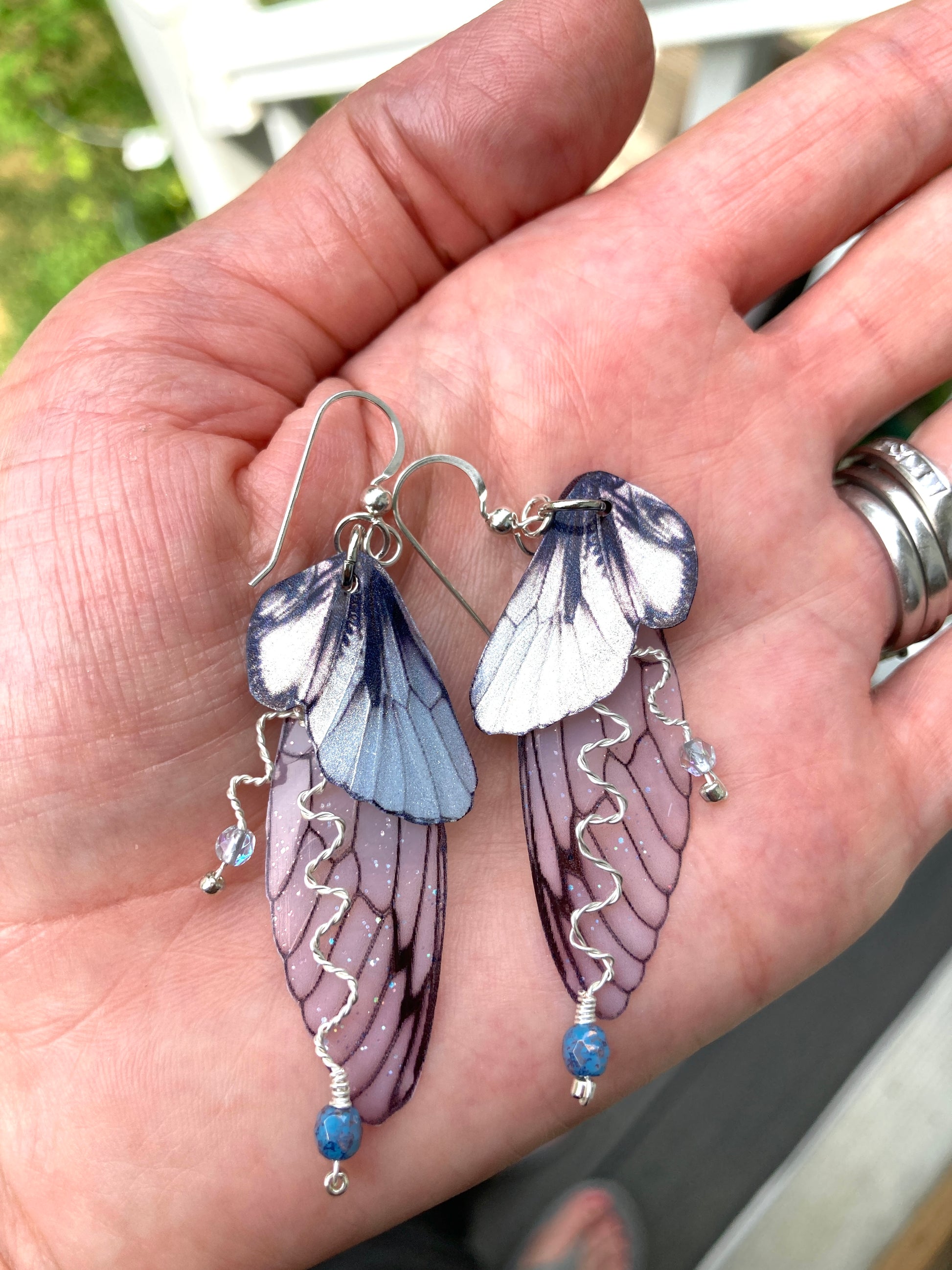 silver double wing fairy earrings with silver twisted wired branches with crystals laying flat in a hand