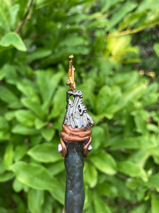 Profile view of dragon hair pin  held vertically in a hand with dragon head breathing fire made from  gold seed beads.