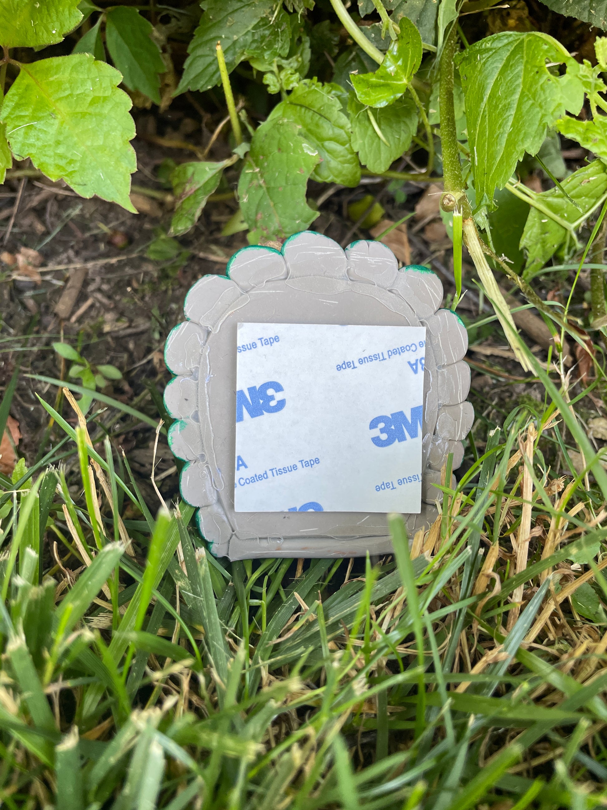 Back of small butterfly fairy door showing a sticky pad for attaching to furniture. The door is sitting on grass in a garden.