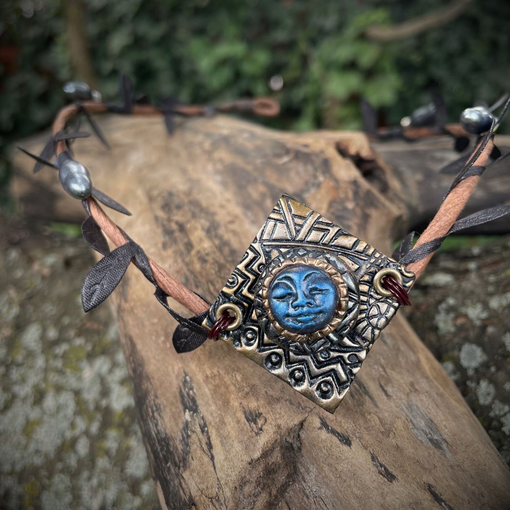 Blue moon on a golden textured diamond shape focal on a brown wire leaf crown resting on a tree branch.