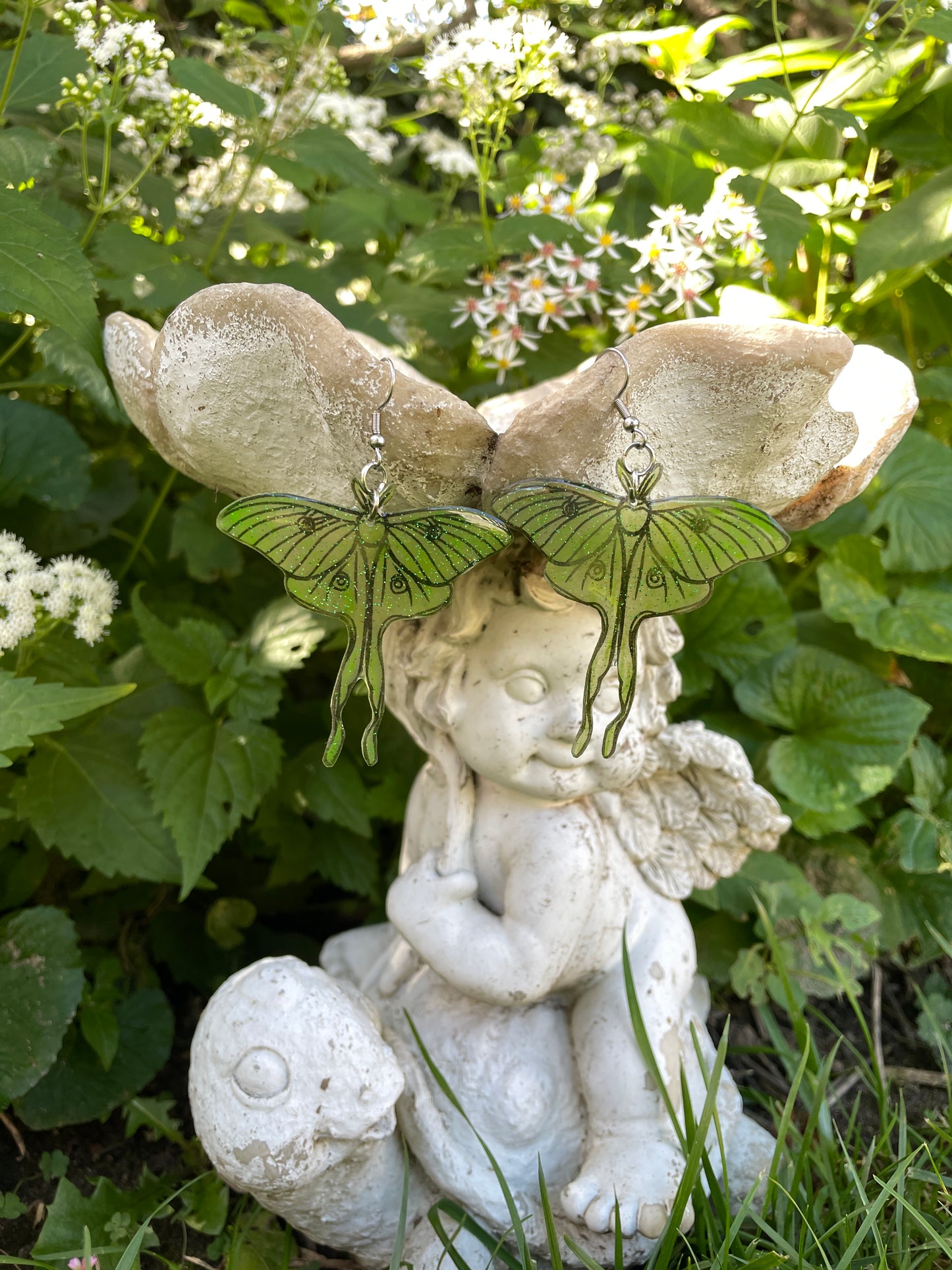 Green luna moth earrings hanging on a garden ornament.