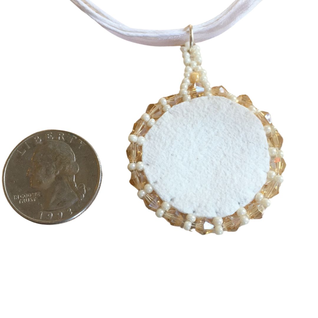 White faux suede of the reverese A golden beaded necklace with topaz crystals on a white cord necklace next to a quarter for size reference.