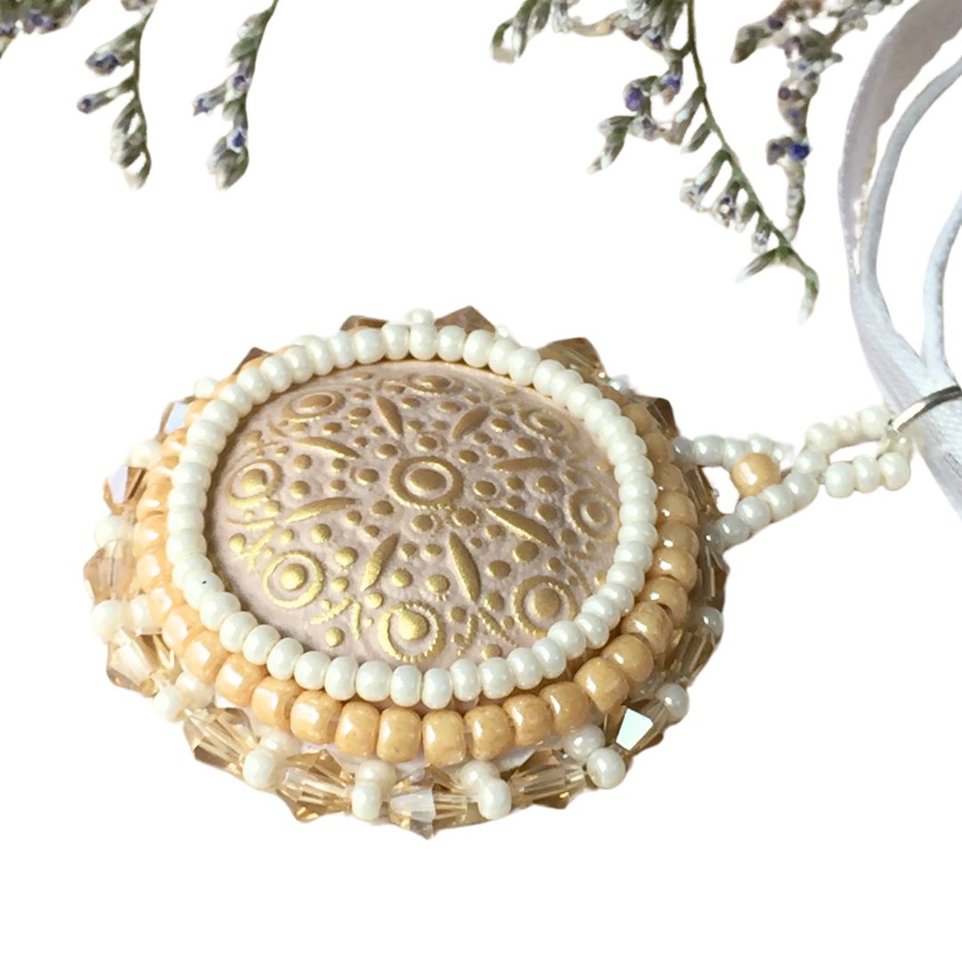 Side profile of a golden beaded necklace with topaz crystals on a white cord necklace.