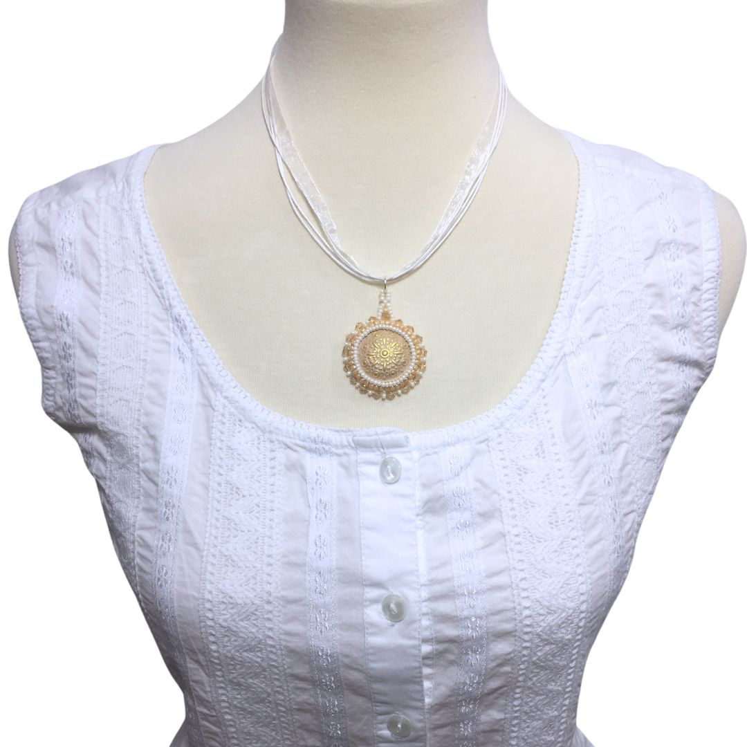 A golden beaded necklace with topaz crystals on a white cord necklace on a model wearing a white top.