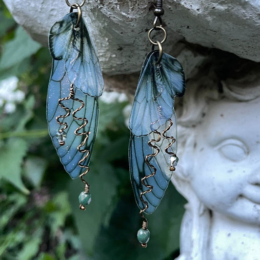 Olive green double fairy wing dangle earrings with antique wired green crystals hanging on a garden ornament.