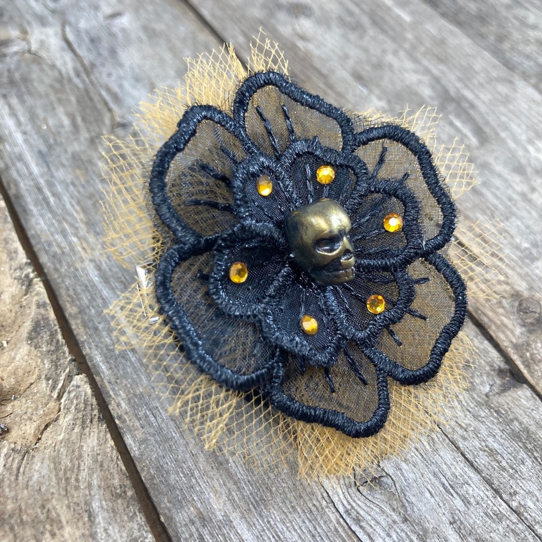 Black flower applique with a gold skull in the center surrounded by orange crystals and orange tulle behind the black flower.