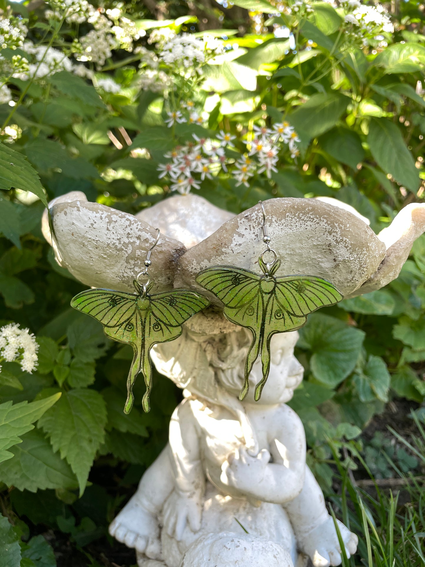 Green luna moth earrings hanging on a garden ornament.