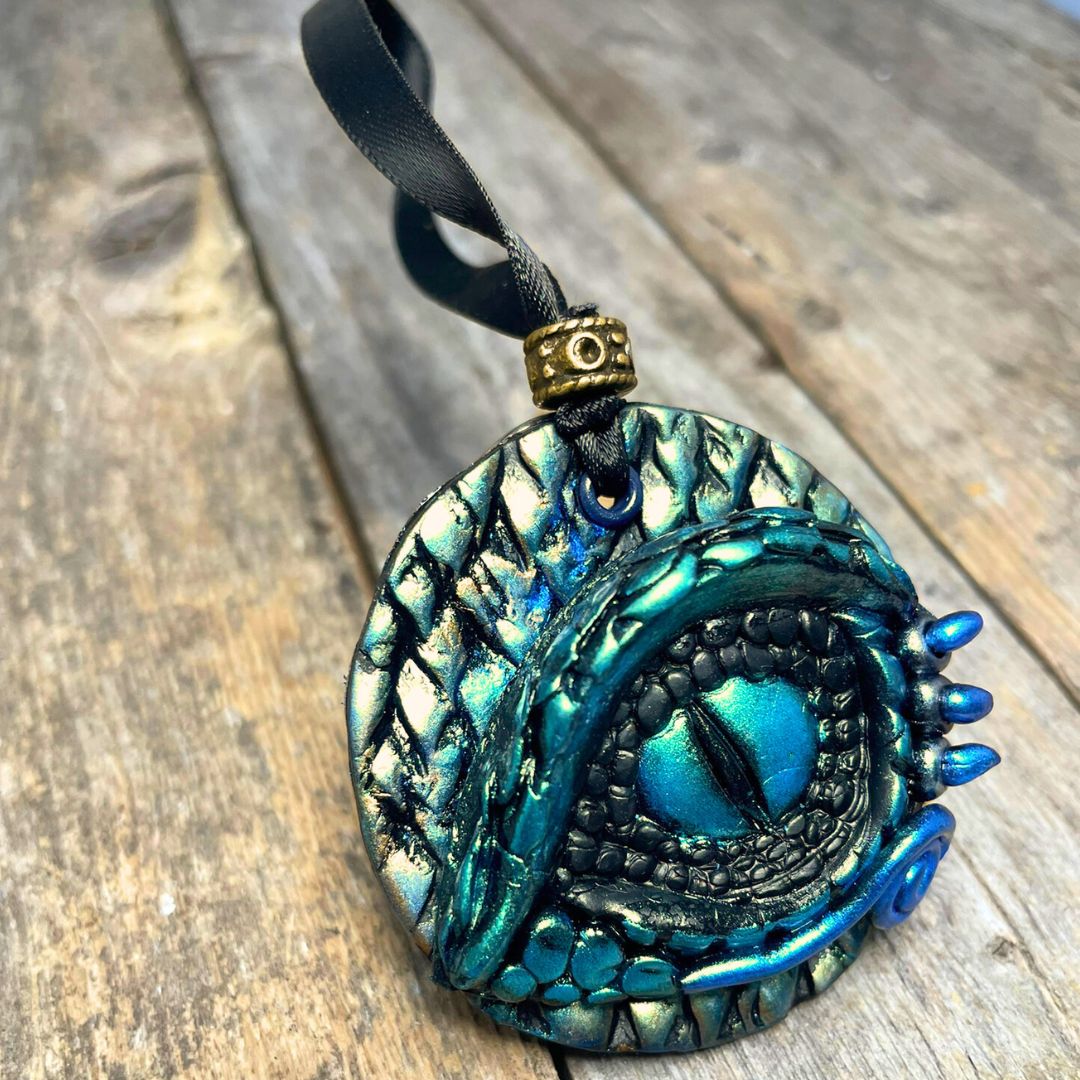 A round dragon eye ornament with metallic green gold and blue coloring with black satin ribbon