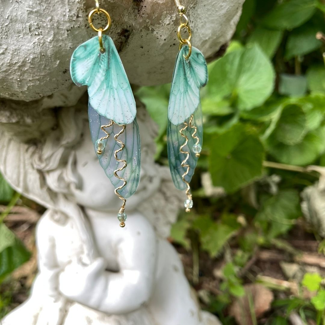 Mint green double wing fairy wings with gold twisted wires with crystals. and gold french ear hooks hanging on a angel garden ornament.