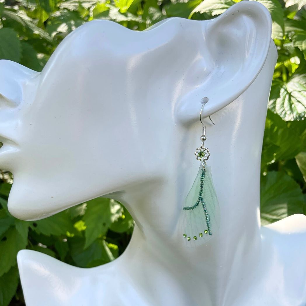 Green sheer fabric beaded butterfly wing earrings with green crystals with a flower bead connecting to the ear wires. on a model