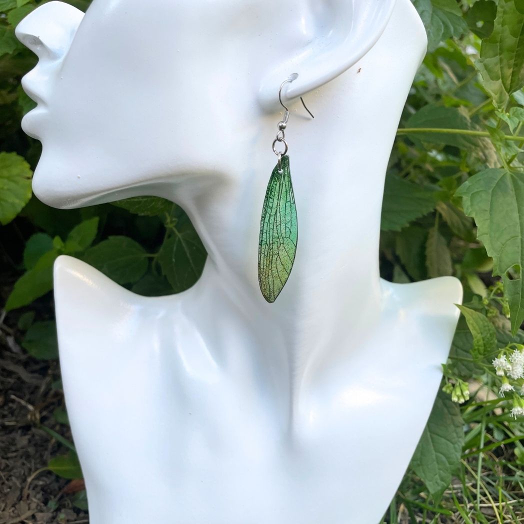 Sparkly glitter green dragonfly wing earrings on a bust.