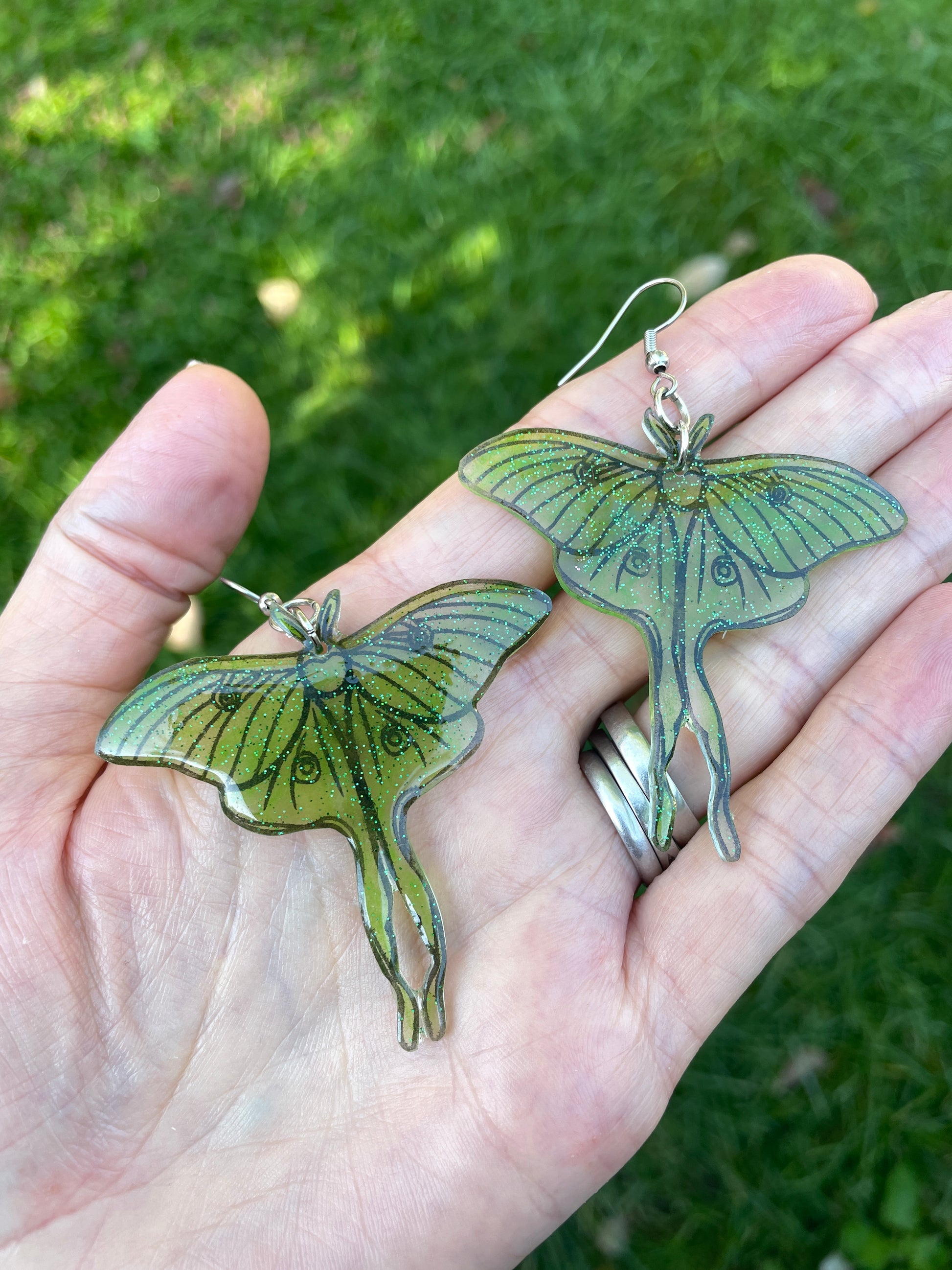 Green luna moth earrings held in a hand.