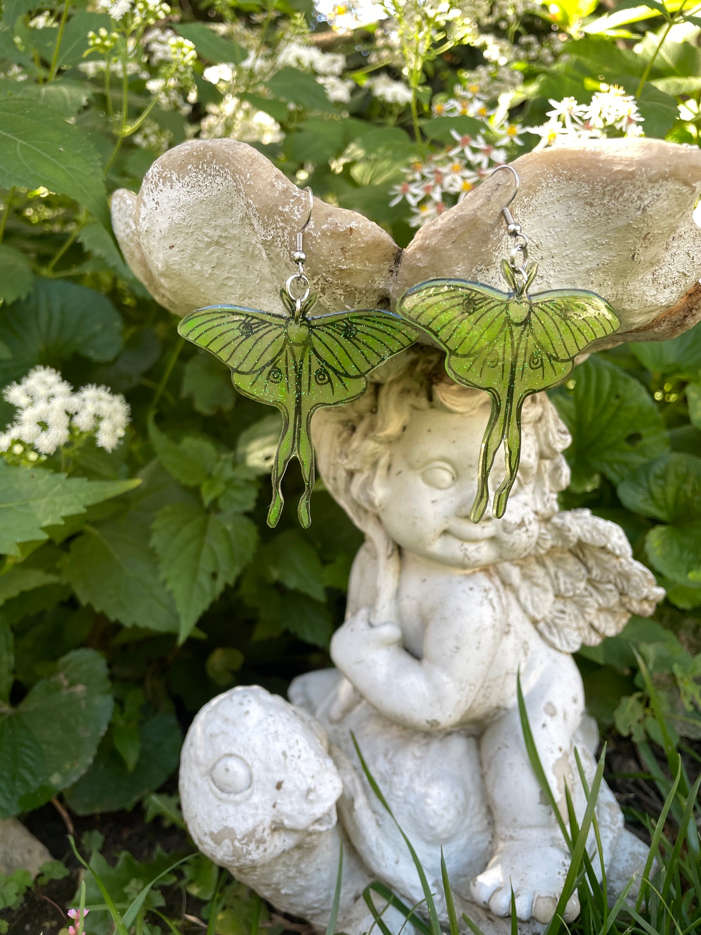 Green luna moth earrings hanging on a garden ornament.