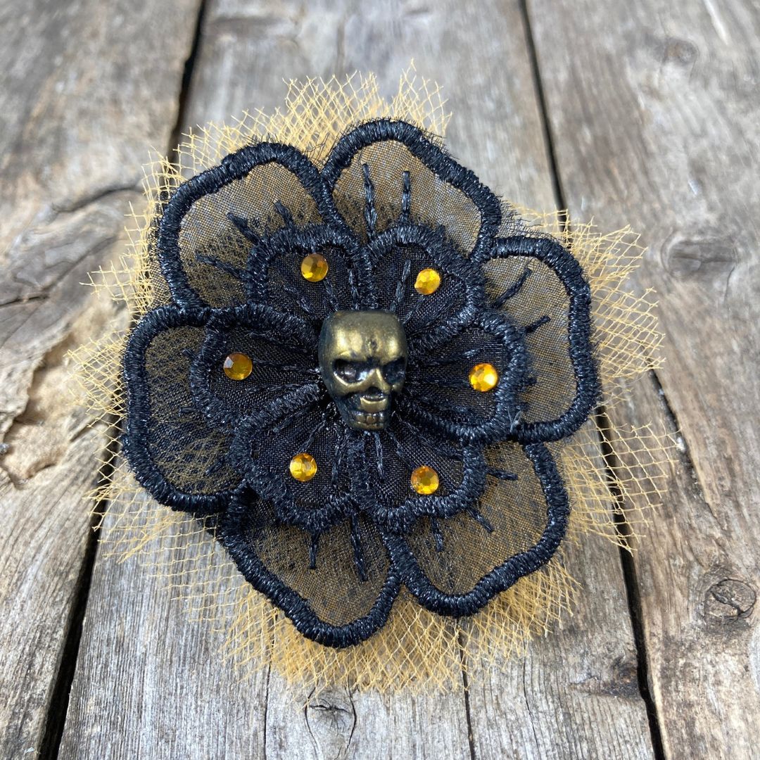 Black flower applique with a gold skull in the center surrounded by orange crystals and orange tulle behind the black flower.