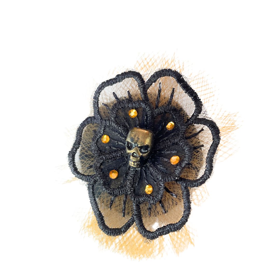 Black flower applique with a gold skull in the center surrounded by orange crystals and orange tulle behind the black flower.