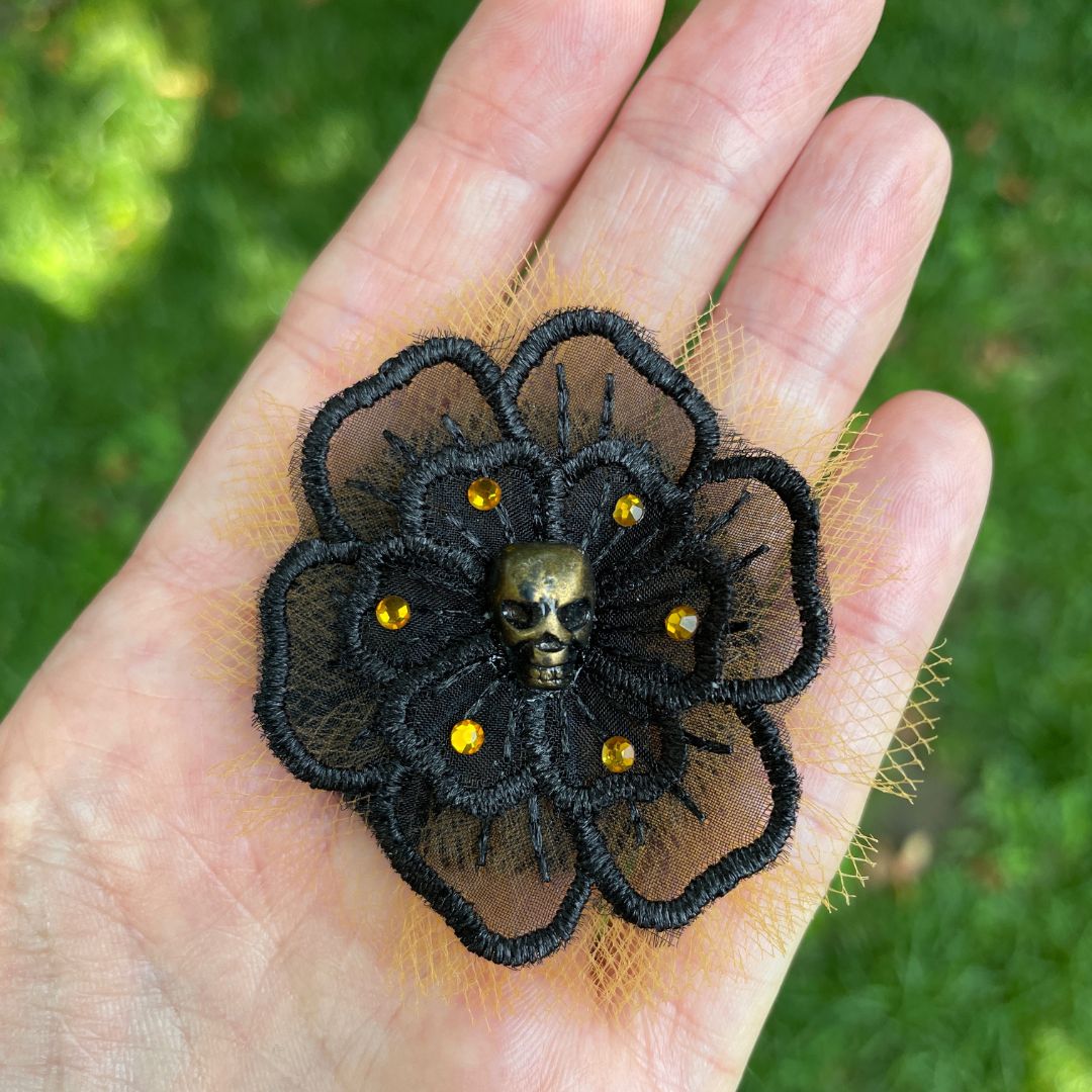 Black flower applique with a gold skull in the center surrounded by orange crystals and orange tulle behind the black flower in hand.