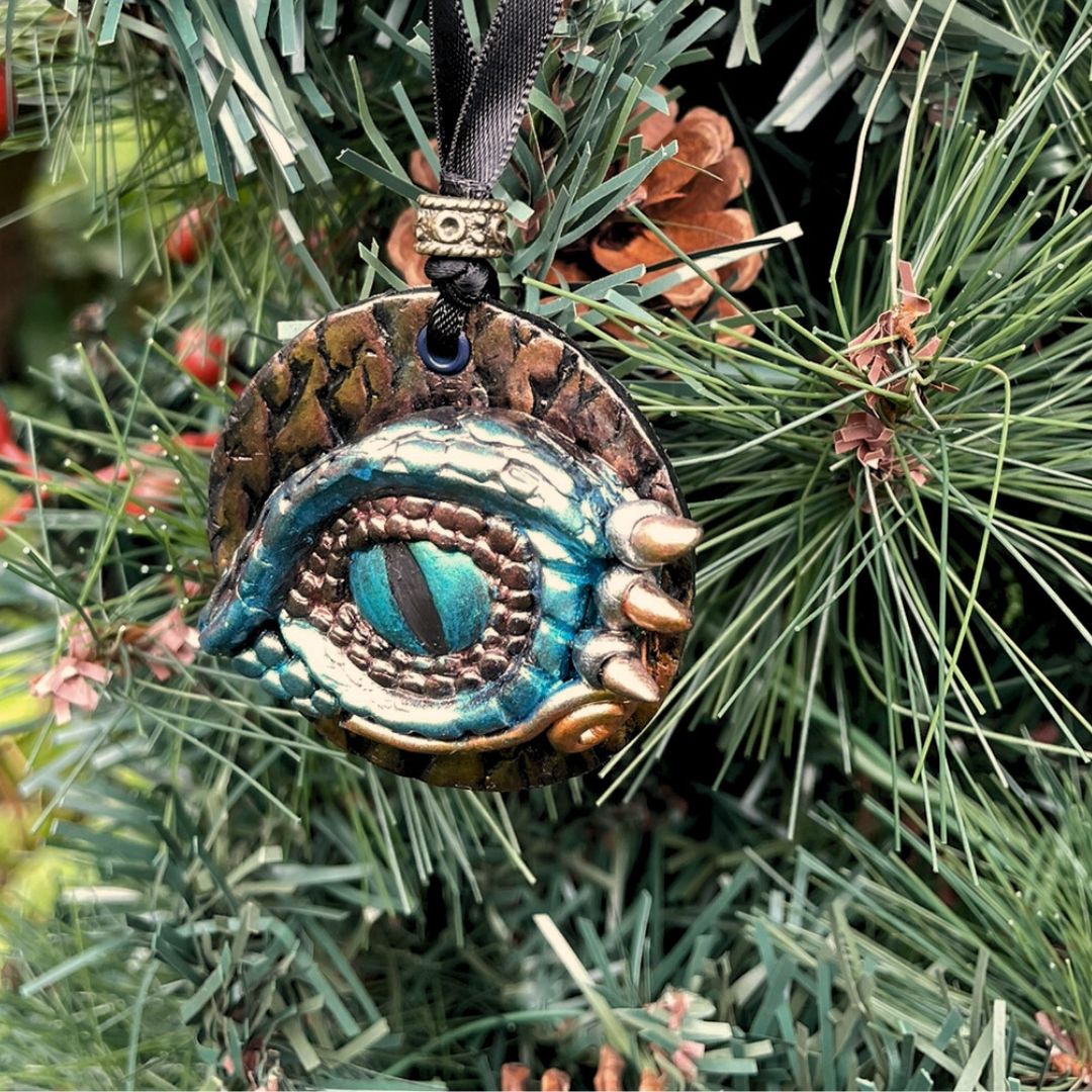 A round dragon eye ornament with metallic green gold and bronze coloring with black satin ribbon hanging on a Christmas Tree