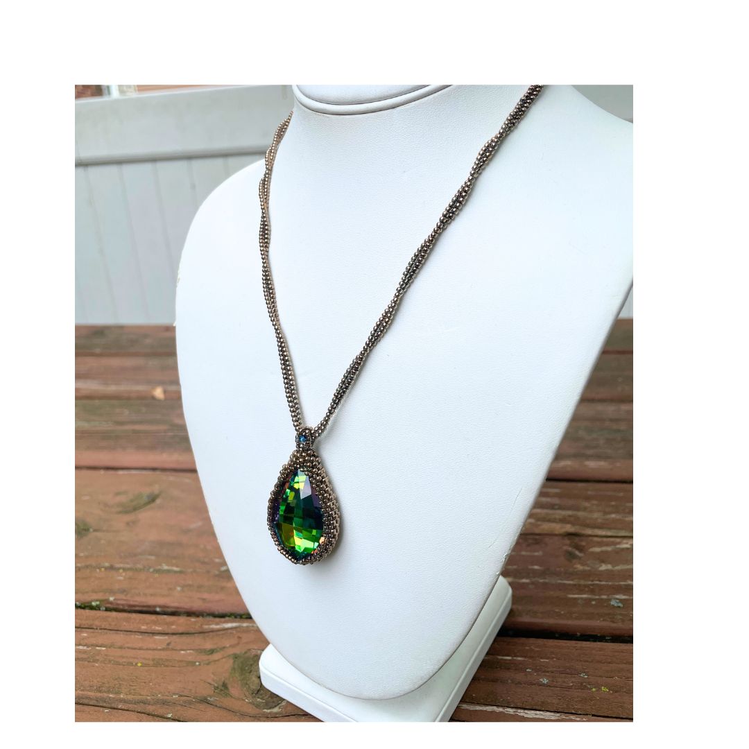 large beaded teardrop shaped rainbow crystal necklace with twisted beaded chain with an iridescent button closure on a display bust.