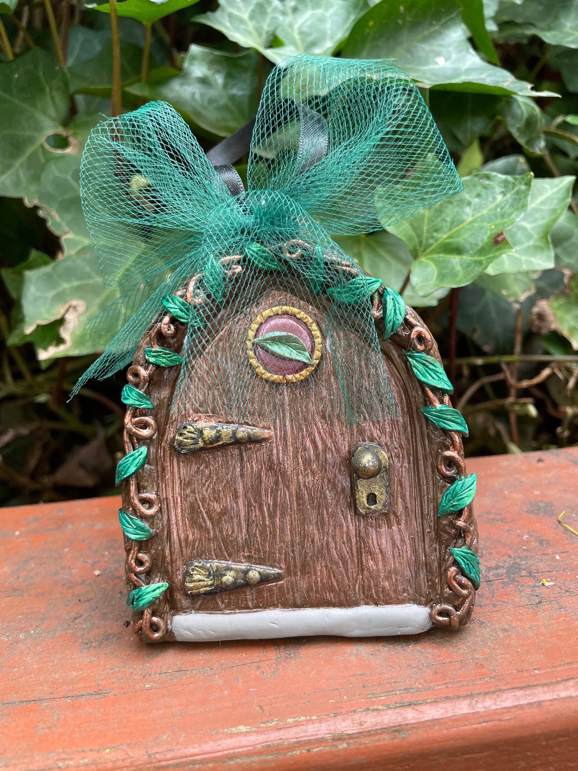 Fairy door ornament with vines and green tulle bow in a garden setting.