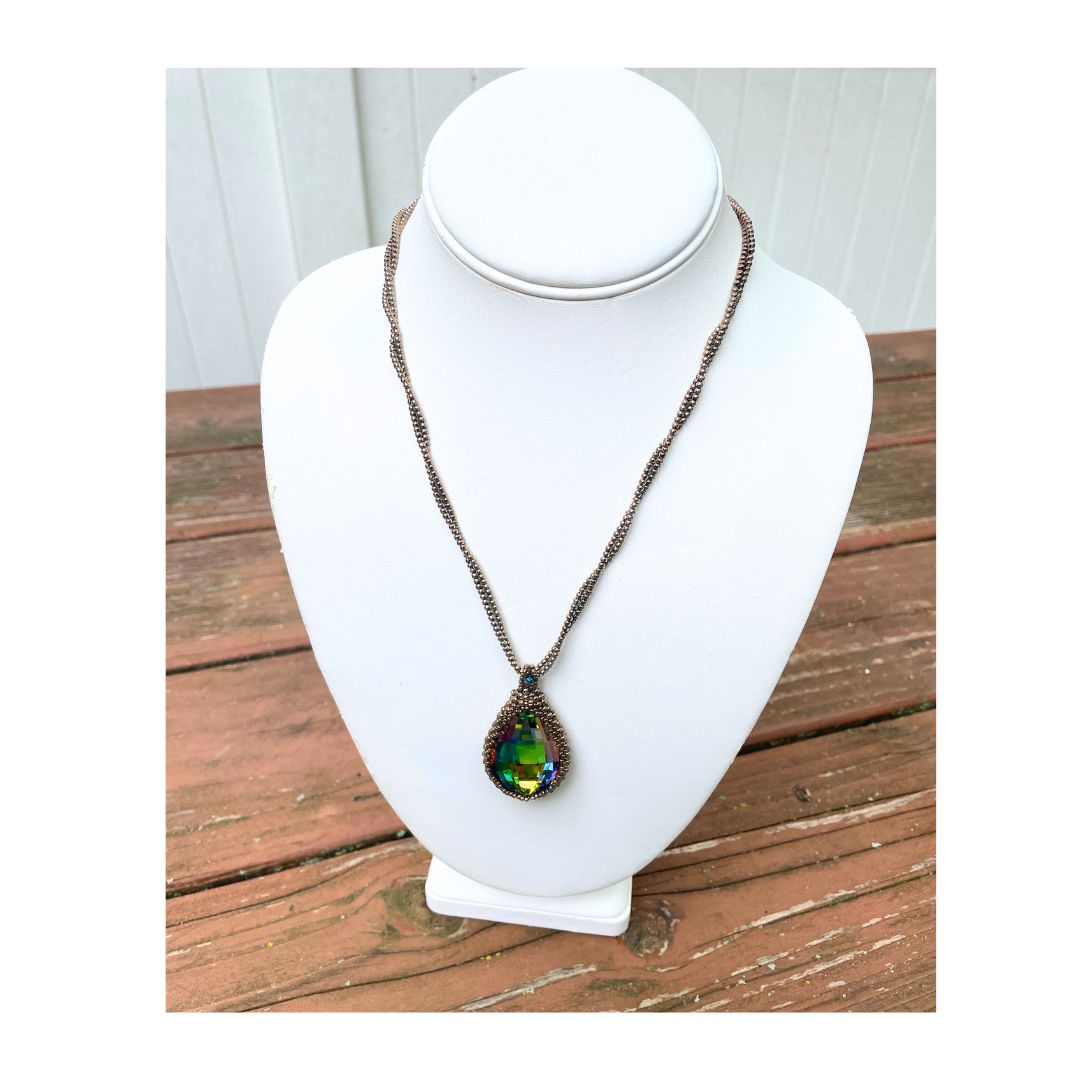 large beaded teardrop shaped rainbow crystal necklace with twisted beaded chain with an iridescent button closure on a display bust.