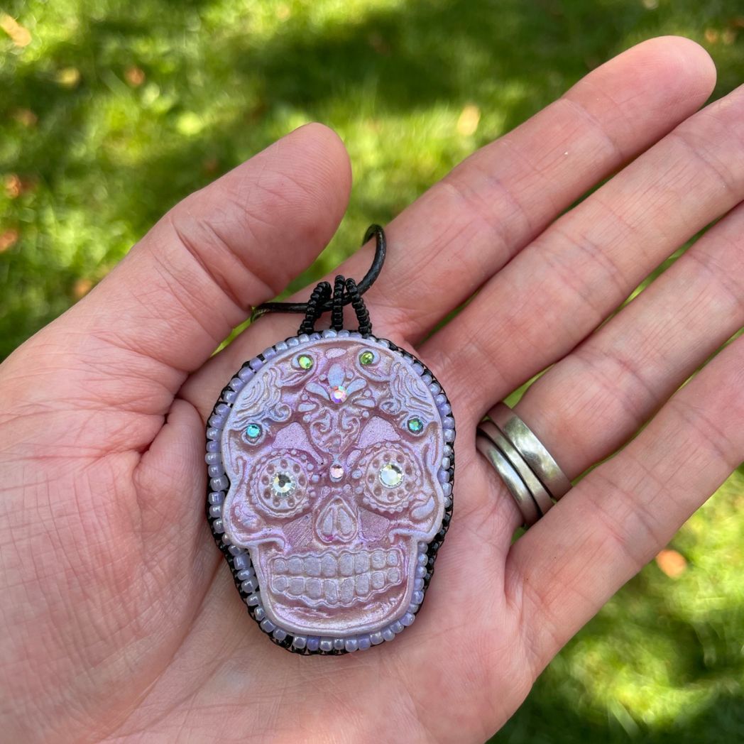Pink sugar skull necklace  with colorful crystal details with seed beaded edging and black cord necklace. Held in hand for size reference