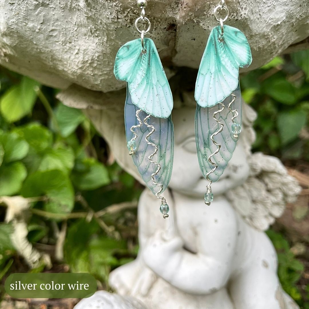 Mint green double wing fairy wings with silver twisted wires with crystals. and silver french ear hooks hanging on a angel garden ornament.