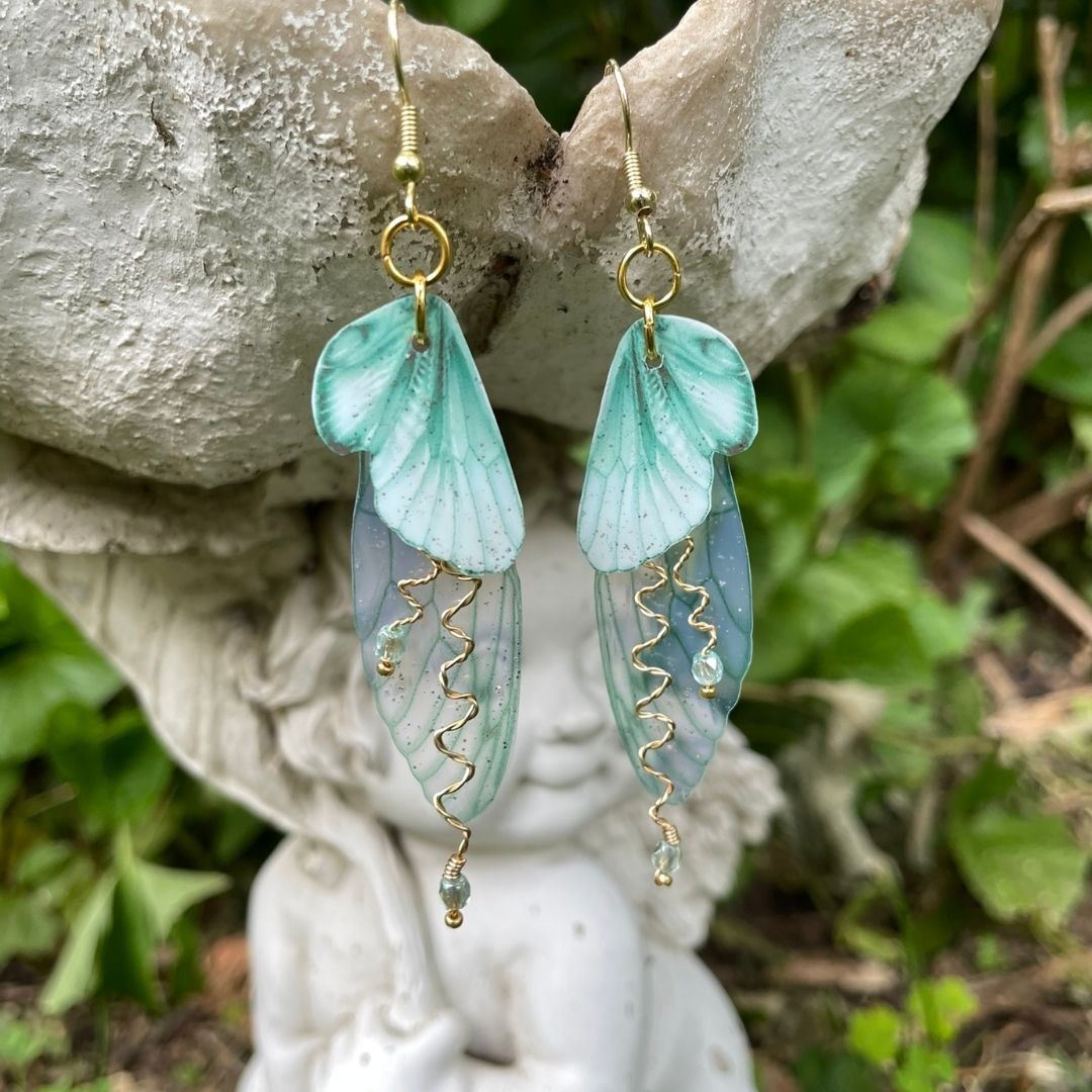 Mint green double wing fairy wings with gold twisted wires with crystals. and gold french ear hooks hanging on a angel garden ornament.