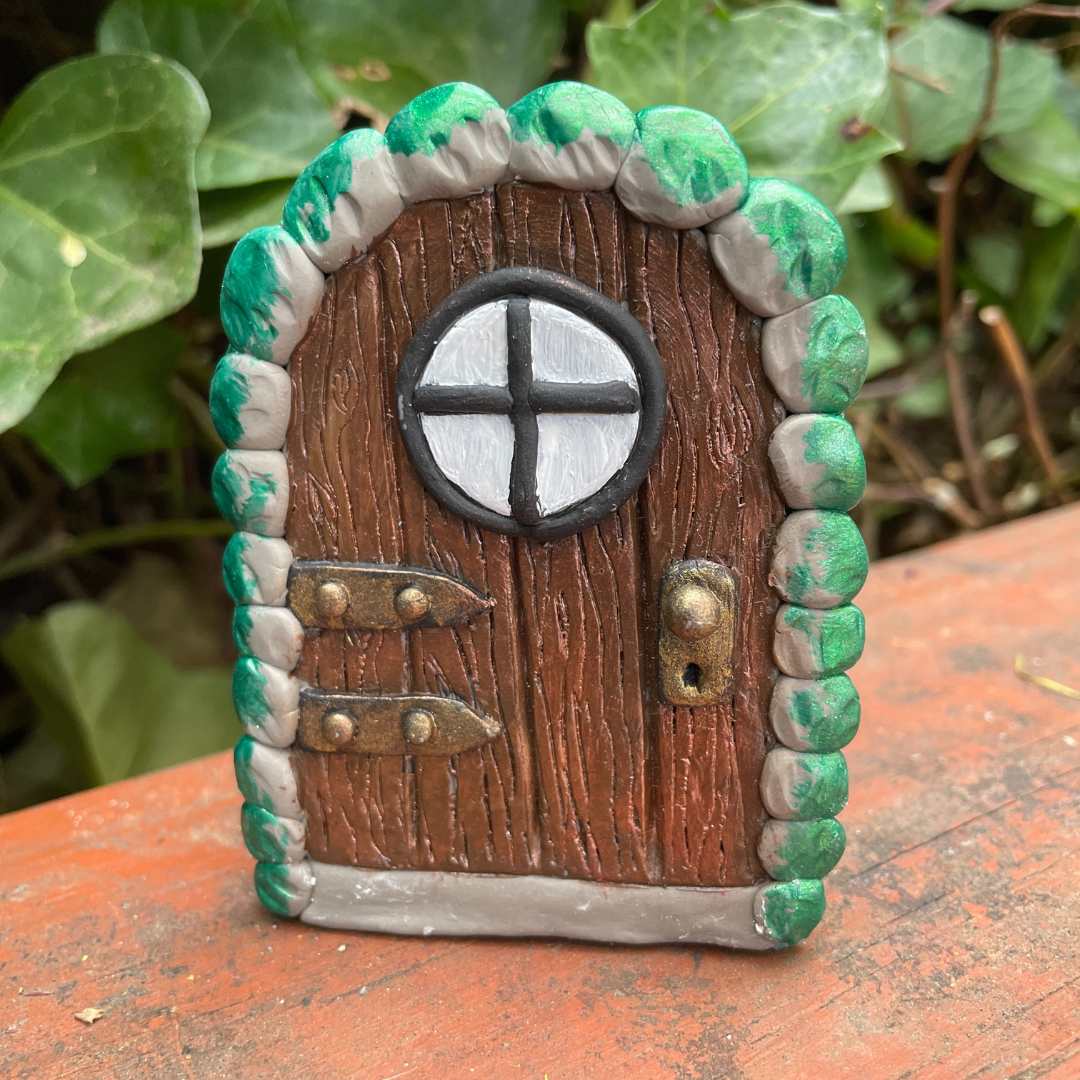 miniture arched elf door ornament with a  against green plants and purple flowers.